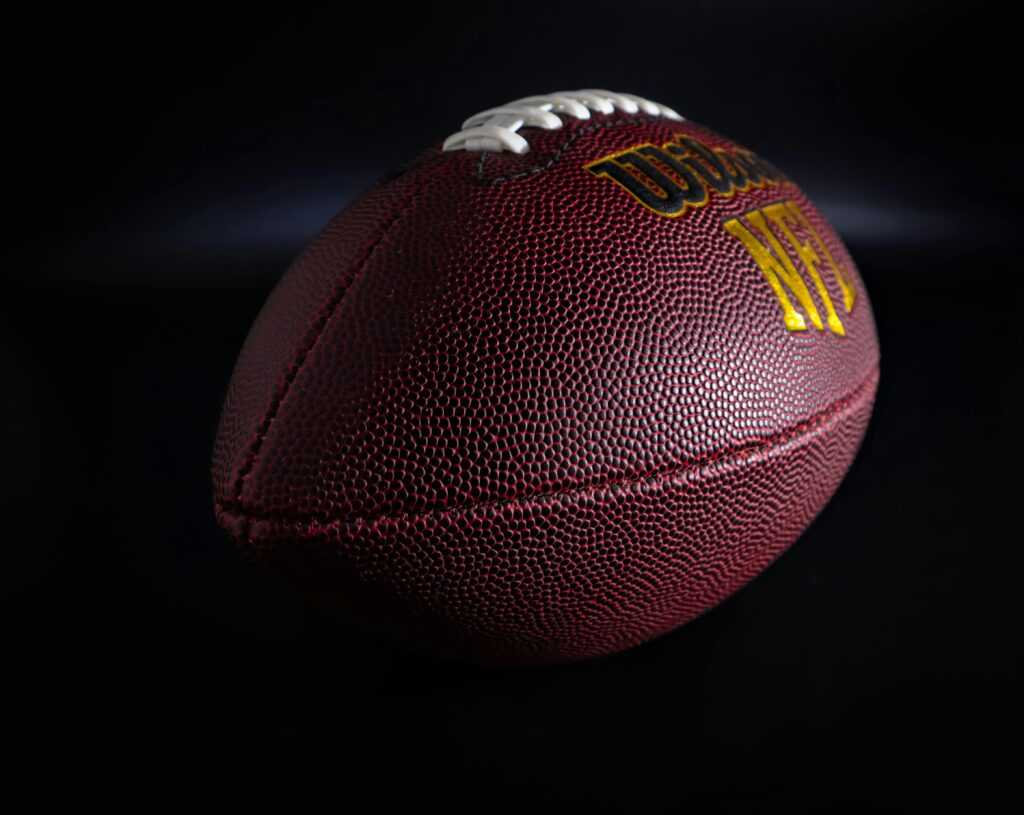 Detailed view of a traditional brown and white American football against a dark backdrop, highlighting texture.